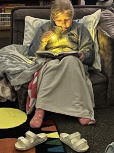 Girl sitting in a chair reading with a flashlight