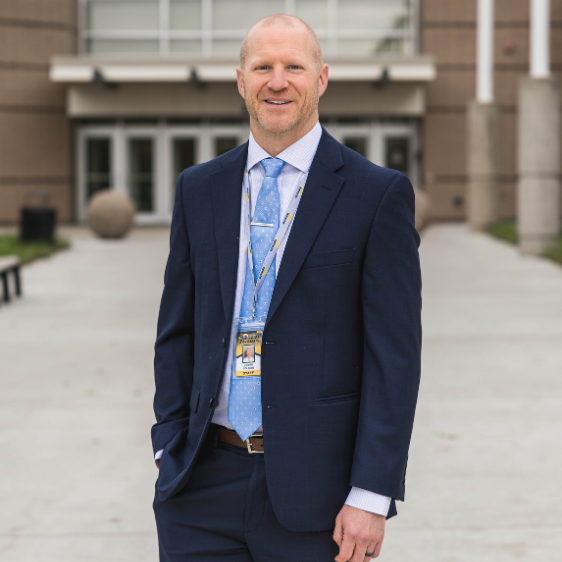 A photo headshot of Dr. Colbert, standing in front of SEP High School.
